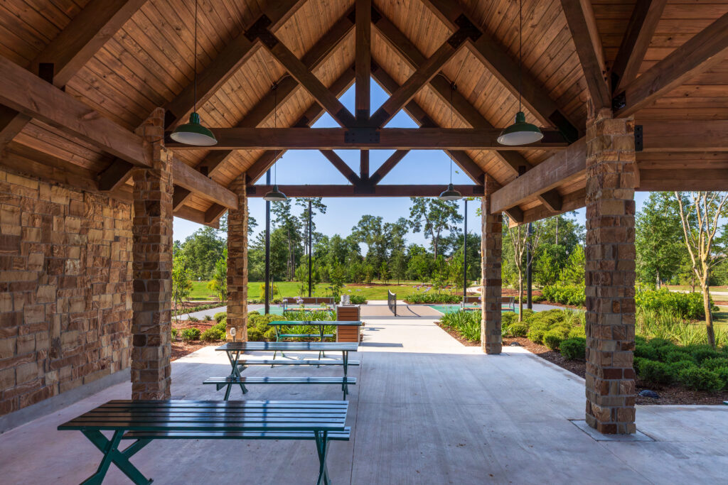 Open-air pool pavilion with a large timber canopy providing shaded picnic and gathering space for neighborhood residents.